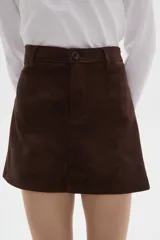 Falda mini de gamuza en color marrón, con diseño de cintura alta, cierre frontal con botón y presillas para cinturón.