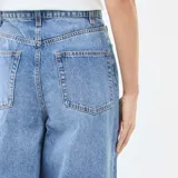 Jean de corte wide leg y tiro alto, confeccionado en denim azul. Presenta pinzas en la cintura, cierre frontal con botón y bolsillos laterales.