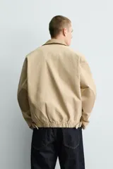 Cazadora relaxed fit de Zara confeccionada en denim de algodón color beige, con cuello de solapa en piel combinada, bolsillos con cremallera en el pecho y cierre frontal oculto.