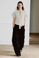 Blusa de viscosa con estampado de lunares, cuello redondo con escote en pico, volantes y lazada frontal. Presenta manga corta y bajo recto.