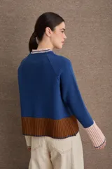 Cardigan de punto con diseño color block en tonos bordó, verde oliva y beige. Presenta cuello redondo con detalle en celeste, cierre frontal con botones y puños acampanados en color beige.