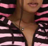 Collar de cadena fina plateada con un dije colgante de metal plateado con forma ovalada y texturizada, similar a un candado abierto o una piedra pulida.