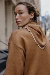 Jersey de punto color marrón, manga larga y corte holgado, con cuello tipo bandana anudado y terminaciones con puntilla blanca a contraste.