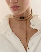Choker tipo bolo tie confeccionado en tiento de cuero marrón, con dije central ovalado de acrílico espejado con diseño de estrella calada y terminales metálicos dorados.