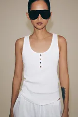 Top de algodón blanco con escote redondo, sin mangas y cierre frontal con pequeños botones. Presenta un diseño acanalado y bajo redondeado.