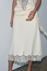 Falda midi de punto liso color crema, con cintura elástica y bajo acampanado. El ruedo está decorado con bordados, abalorios y encaje a tono.