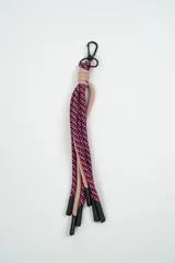 Llavero de cordón trenzado multicolor con patrón geométrico en tonos fucsia, negro, gris y naranja, equipado con un gancho mosquetón metálico negro.