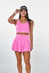 Conjunto deportivo compuesto por un top de cuello redondo y una pollera short con diseño plisado, ambos en color fucsia. El top presenta un logo estampado en el frente.