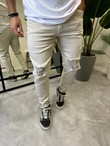 Jean de corte skinny color arena con roturas y desflecados en las rodillas.