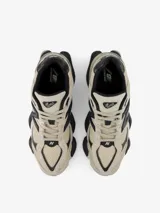 Championes urbanos New Balance modelo 9060, de color gris y beige con detalles en negro. Presentan un diseño robusto y futurista inspirado en la era Y2K, con entresuela gruesa esculpida y el característico logotipo "N" en el lateral.
