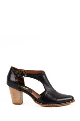 Zapato guillermina artesanal de cuero negro, con taco alto de madera, puntera redondeada y tira en T con hebilla metálica ajustable en el lateral.