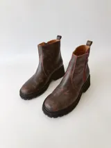 Botas cortas de cuero color chocolate, con elástico lateral, cierre interno con cremallera roja, pespuntes rojos y suela track.