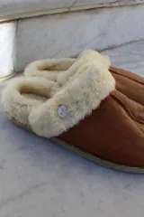Pantufla de cuero color habano con interior de piel sintética, suela de goma y detalle de costura central.