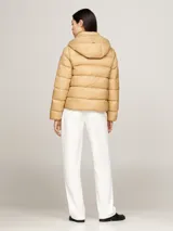 Campera puffer color beige, con capucha y cierre frontal con cremallera. Tiene dos bolsillos delanteros con botón a presión y parche con el logo de Tommy Hilfiger en la manga.