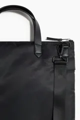 Bolso tote negro de tejido revestido con doble asa superior y correa bandolera ajustable y extraíble. Cuenta con compartimento principal con cierre y bolsillo frontal con costura vertical y botones a presión decorativos.