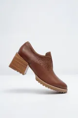 Zapato de cuero color marrón, con tacón de madera y suela dentada. Presenta detalles de textura en relieve en los laterales y el empeine.