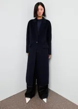 Abrigo largo de corte recto confeccionado en tejido mezcla de lana. Presenta cuello con solapas de muesca, cierre frontal de dos botones y dos bolsillos laterales con solapa.