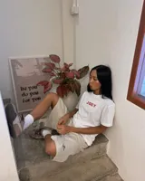 Remera de manga corta blanca con diseño gráfico en la espalda estilo estampilla que muestra una fotografía en blanco y negro de una persona con un gato, acompañada del logotipo rojo de Kaboa Industries.