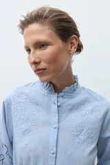Camisa blanca de manga larga con cuello alto fruncido y bordados calados en el pecho y los hombros.