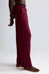 Pantalón de franela de algodón suave con estampado a cuadros en tonos rojos y negros. Presenta cintura elástica con cordón ajustable, cierre decorativo y bolsillos laterales al bies.