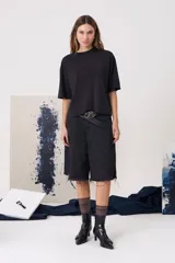 Bermuda de denim negro con tiro medio, cierre frontal con botón metálico, bolsillos laterales y traseros, y terminación desflecada en el ruedo.