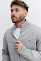 Cardigan de punto color azul marino, con cierre frontal completo, cuello alto y puños acanalados. Presenta un pequeño bordado distintivo en el pecho.
