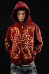 Hoodie con cierre frontal, color bordó, con estampado serigráfico en color dorado que recorre el frente y las mangas con un diseño inspirado en hojas de acanto. Cuenta con bolsillos laterales y cierre metálico.