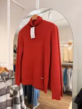Polera de cuello alto en color terracota, confeccionada con un interior suave y cálido. Presenta puños y ruedo acanalados, con un pequeño aplique metálico decorativo en la parte inferior.