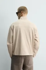 Sudadera de algodón color beige claro con efecto lavado, corte relajado, cuello alto y cierre frontal de cremallera. Presenta bolsillos de vivo en la cadera y mangas largas.