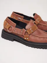 Mocasines de cuero negro con plataforma, diseño tipo náutico con costuras reforzadas en la puntera, detalle de tira sobre el empeine con apliques metálicos y argollas laterales.