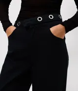 Pantalón de jean corte wide leg, color negro, con cintura media y detalle de ojales metálicos en el cós. Presenta piernas amplias, cierre tradicional y bolsillos funcionales.