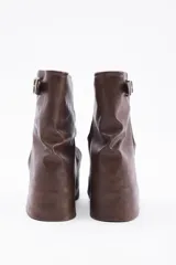 Botas de caña media confeccionadas en cuero vegano color negro, con diseño de solapa frontal y detalle de hebilla metálica en la parte superior.