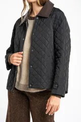Campera negra de diseño capitoneado con cuello de solapa en contraste color marrón. Presenta cierre frontal con cremallera y botones a presión, mangas largas con puños ajustables y un corte recto.