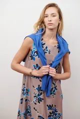 Vestido midi color beige con estampado de hojas en tonos violeta, verde y negro. Diseño sin mangas, con escote redondo y falda acampanada.