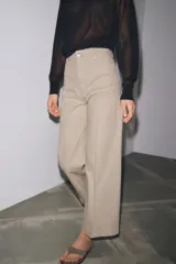 Jeans de tiro alto y pierna ancha de Zara, confeccionados en mezcla de algodón color beige. Presentan cintura con trabillas, bolsillos de parche en la espalda, costuras frontales marcadas y cierre delantero con cremallera, botón y gancho metálico.