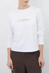 Remera de manga larga color blanco, con cuello redondo y diseño de bordado lineal en el centro del pecho que representa elementos de desayuno.