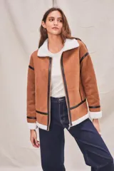 Campera marrón de gamuza sintética con cuello, puños y ruedo de piel sintética blanca. Presenta cierre frontal con cremallera, bolsillos laterales y detalles en cuero sintético negro.