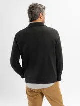 Buzo de tejido de punto en color negro, con cuello tipo polo y cierre frontal parcial. Presenta puños y ruedo acanalados.
