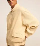 Campera color beige claro de algodón con textura arrugada, cuello inglés, cierre con cremallera, bolsillos laterales, elástico en la cintura y puños.