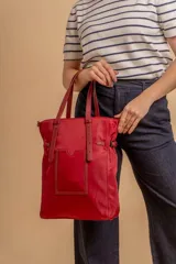 Bolso tipo tote bag de símil cuero color rosa pálido, con asas dobles y detalles de costura en color beige claro. Presenta un bolsillo frontal rectangular aplicado y herrajes metálicos.