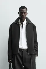 Sobrecamisa relaxed fit de Zara confeccionada en tejido negro con estructura diagonal. Presenta cuello subido, manga larga, bolsillos de vivo en la cadera y cierre frontal con cremallera.