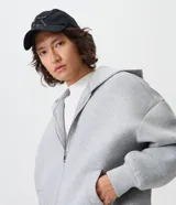 Campera boxy de malla scuba color gris melange, con capucha, cierre frontal completo y bolsillos laterales ocultos.