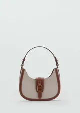 Bolso tipo hobo de lona color crema con ribetes de cuero marrón y cierre con hebilla dorada.