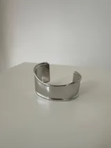 Brazalete rígido tipo cuff de diseño minimalista, confeccionado en acero quirúrgico con acabado pulido brillante.