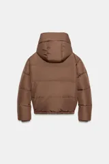 Campera puffer acolchada de color negro, con cuello envolvente, capucha integrada, manga larga, bolsillos laterales ocultos y bajo con elástico. Cierre frontal con botones a presión ocultos por solapa.