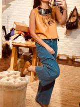 Collar babero de cuero color camel con flecos y detalles de cuentas de madera. Tiene un cuello negro con costuras cruzadas.