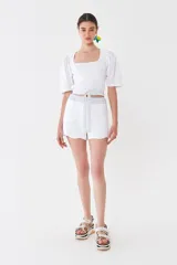 Top blanco tejido en hilado liviano con escote recto y mangas balloon de poplín 100% algodón. Tiene tiras tejidas para ajustar en la cintura.