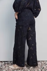 Pantalón largo negro de encaje con diseño floral calado, de tiro alto y corte recto.