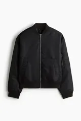 Campera bomber negra, ligeramente acolchada, confeccionada en nylon. Presenta cuello elevado acanalado, cierre frontal, bolsillos al bies con botón a presión oculto, bolsillo con cierre en una manga y dos bolsillos interiores con botón a presión. Los puños y el bajo son de remate acanalado ancho.