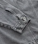 Campera de jean gris con efecto desteñido, corte oversized, cuello inglés, cierre frontal con botones niquelados y aplicaciones de brillos y piedras en la parte superior delantera.